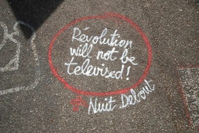 Kreidekreis auf der Straße in dem steht: "Die Revolution wird nicht im Fernsehen übertragen."